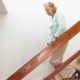 Alte Dame geht eine Holztreppe in ihrem Einfamilienhaus herunter.