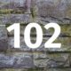 Eine weiße Zahl 102 vor einer Steinwand - Zahl des Monats 102